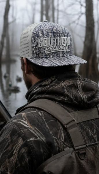 Hunter in a Southern Prodigy camo hat standing in foggy flooded timber with decoys on the water